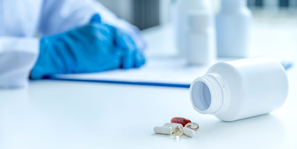 Medicine pill and bottle in front of doctor or pharmacist with a prescription at the pharmacy office, healthcare and medical check-up concept.